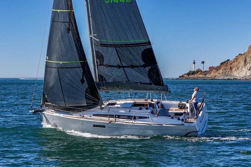The Image of 2022 Jeanneau Sun Odyssey 349 sailing near a rocky coastline with a lighthouse in the background. - 0