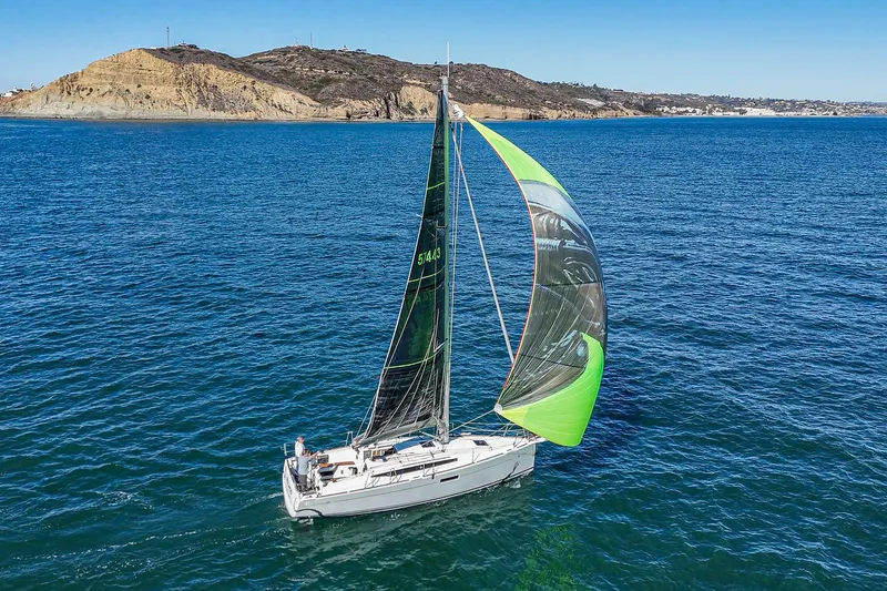 Slide: The Image of Jeanneau Sun Odyssey 349 sailing near rocky coastline, 2022 model, vibrant spinnaker, clear blue water. - 3