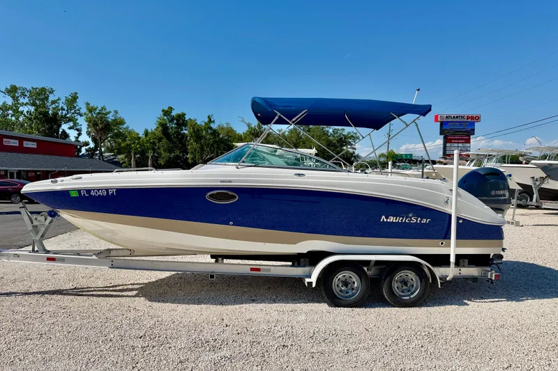 The Image of 2014 NauticStar 243DC Sport Deck boat on trailer, blue and white, parked outdoors. - 0