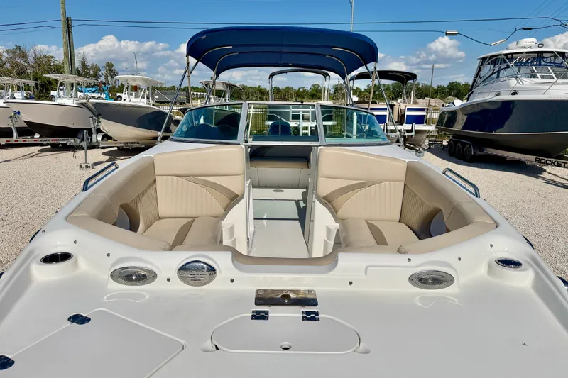Slide: The Image of 2014 NauticStar 243DC Sport Deck boat with beige seating and blue canopy in a marina. - 9