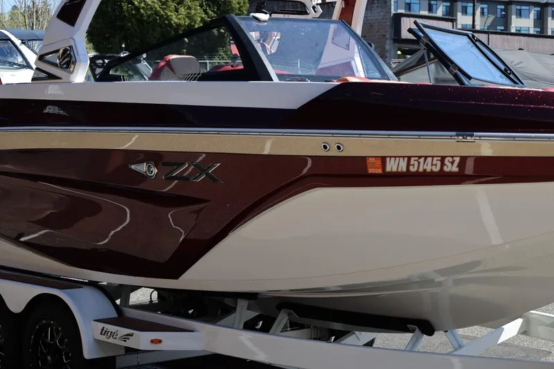 Slide: The Image of 2022 Tigé 25ZX boat with sleek maroon and white design on a trailer. - 10