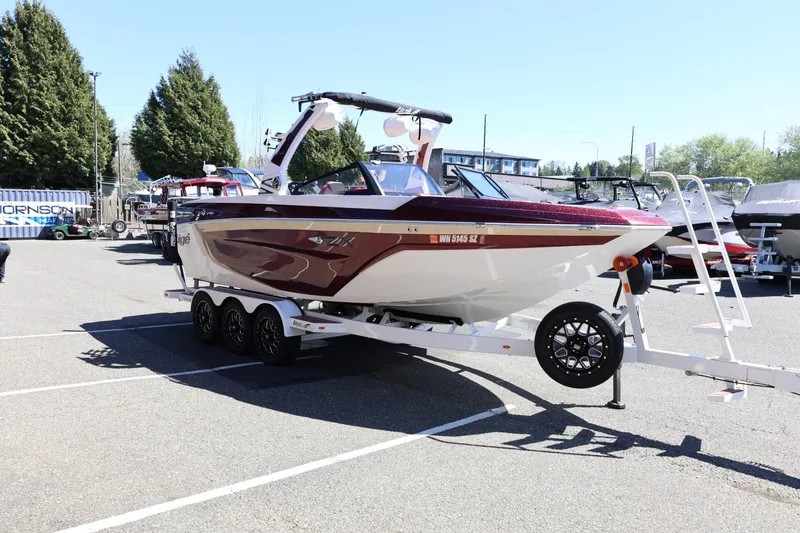 Slide: The Image of 2022 Tigé 25ZX boat on trailer in parking lot, surrounded by trees and other boats. - 11