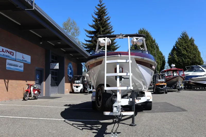 Slide: The Image of 2022 Tigé 25ZX boat on trailer outside dealership, sunny day, surrounded by trees and other boats. - 14