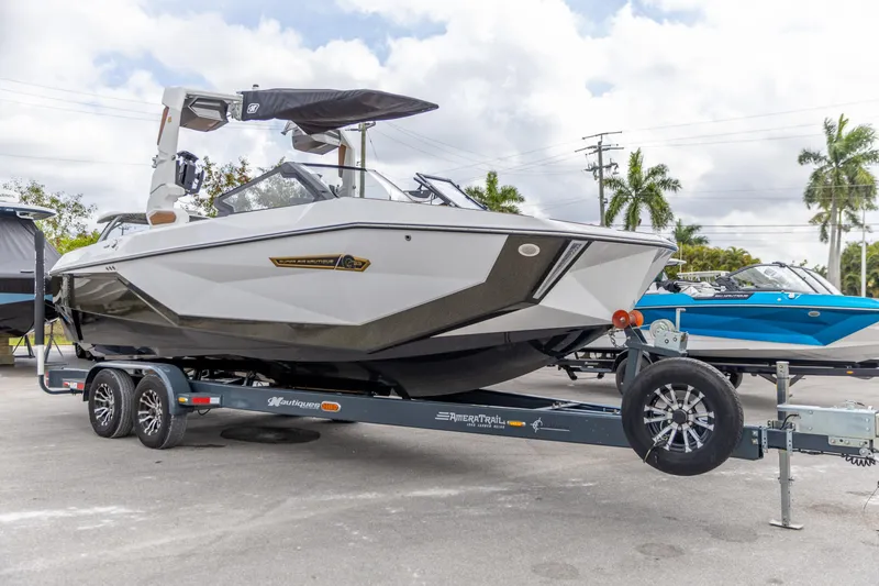 Slide: The Image of 2025 Nautique Super Air Nautique G23 boat on trailer, parked outdoors under cloudy sky. - 19