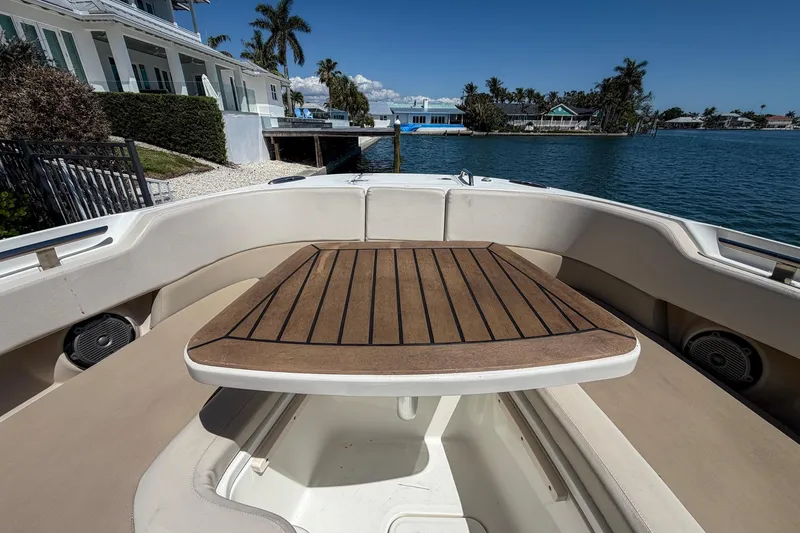 Slide: The Image of 2017 Boston Whaler 320 Vantage boat interior with wooden table, docked by waterfront homes. - 2