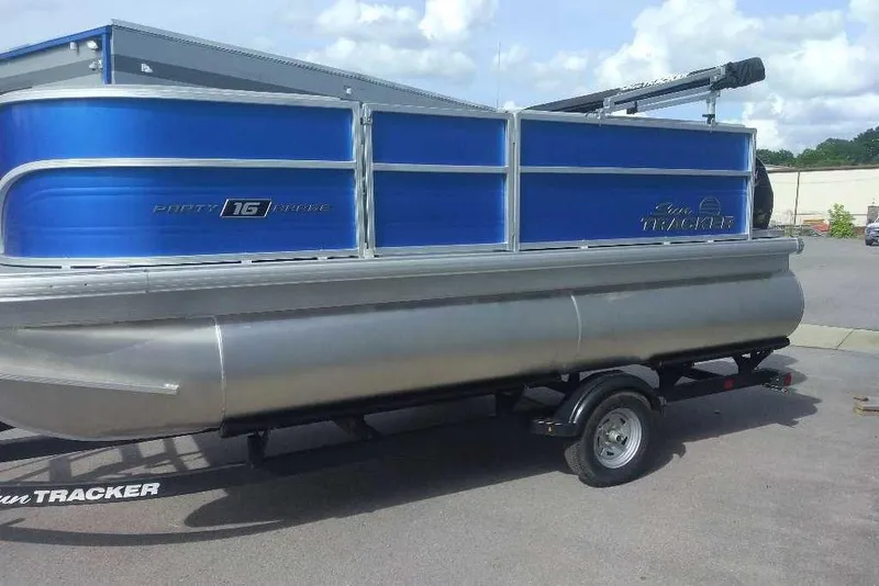 Slide: The Image of 2026 Sun Tracker Party Barge 16 DLX pontoon boat on trailer, blue and silver design. - 1