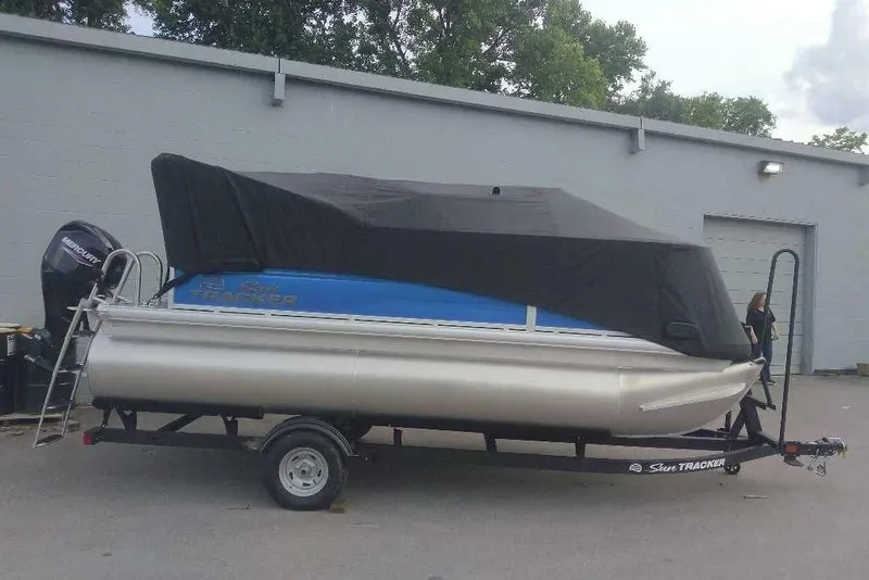 Slide: The Image of 2026 Sun Tracker Party Barge 16 DLX pontoon boat on trailer, covered and parked outdoors. - 2