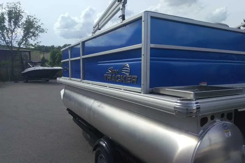 Slide: The Image of 2026 Sun Tracker Party Barge 16 DLX pontoon boat with blue panels in a parking area. - 3