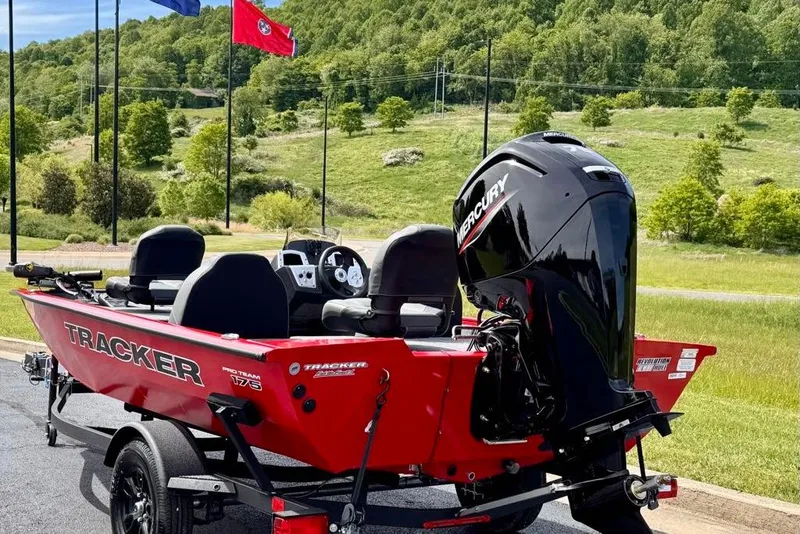 Slide: The Image of 2026 Tracker Pro Team 175 boat with Mercury engine, parked outdoors near flags and greenery. - 6