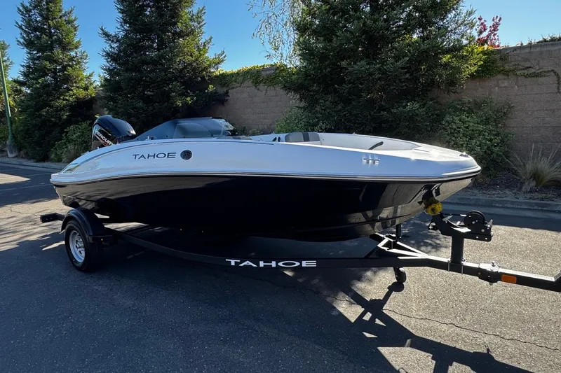 Slide: The Image of 2026 Tahoe T16 boat on trailer, parked outdoors with trees in background. - 2
