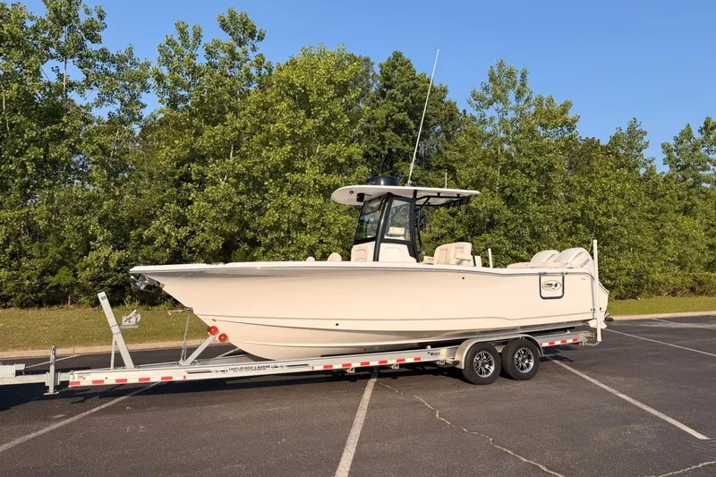 Slide: The Image of 2024 Sea Hunt Ultra 275 SE boat on trailer, parked in a lot with trees in background. - 6