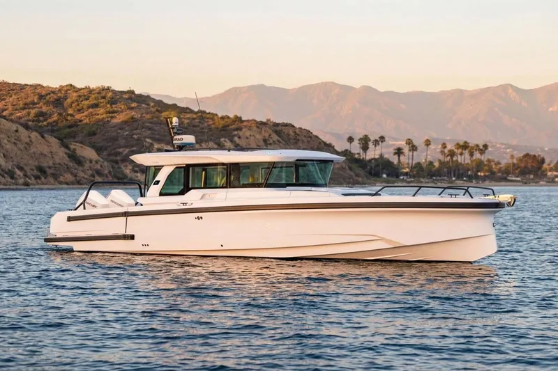 The Image of 2026 Axopar 38 Cross Cabin boat on calm water with scenic mountain backdrop. - 0