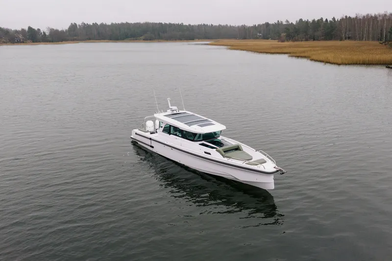 Slide: The Image of 2026 Axopar 38 Cross Cabin boat on calm water, surrounded by forested shoreline. - 11