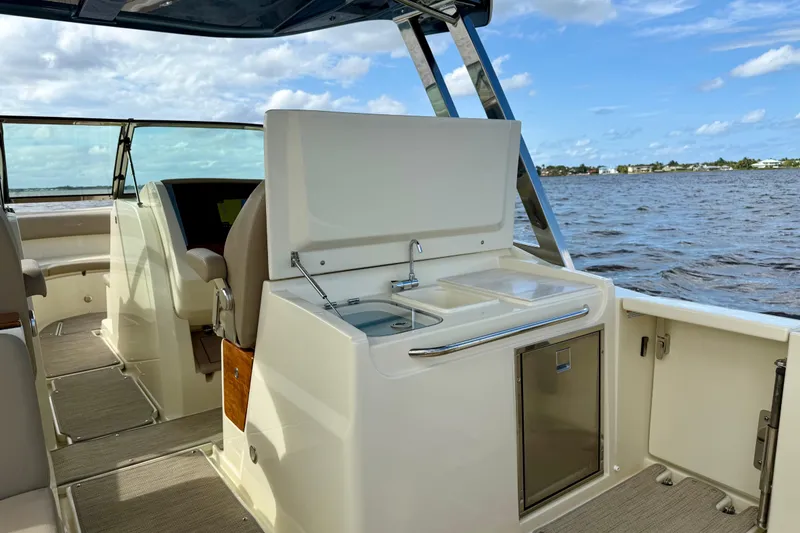 Slide: The Image of 2023 Chris-Craft Calypso 30 boat interior with kitchenette, sink, and seating on a sunny day. - 15