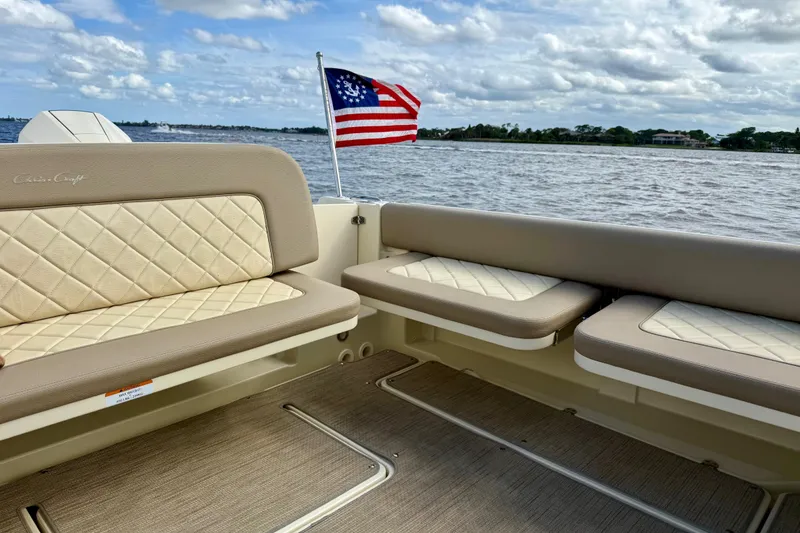 Slide: The Image of 2023 Chris-Craft Calypso 30 boat interior with American flag, beige seating, and ocean view. - 30