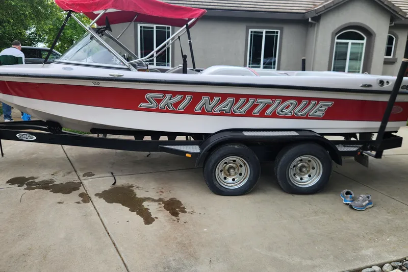 The Image of 2006 Correct Craft Ski Nautique 196 boat on trailer, red and white design, parked on driveway. - 0