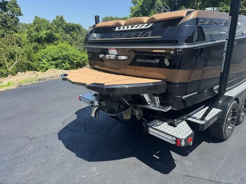 Slide: The Image of 2020 Supra 450 SE boat on trailer, rear view, parked on asphalt with greenery background. - 14