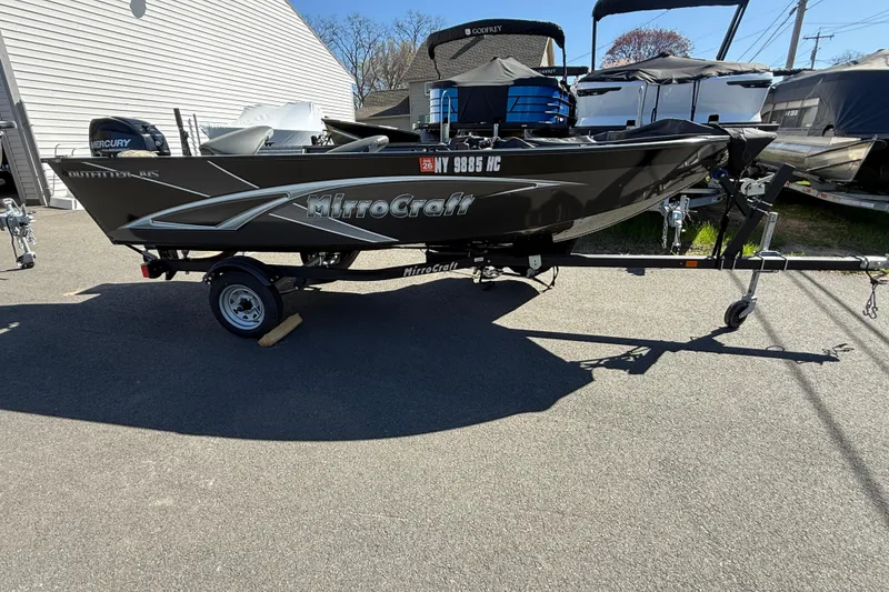Slide: The Image of 2020 MirroCraft 1415 Outfitter boat on trailer, parked outdoors, featuring Mercury engine. - 6