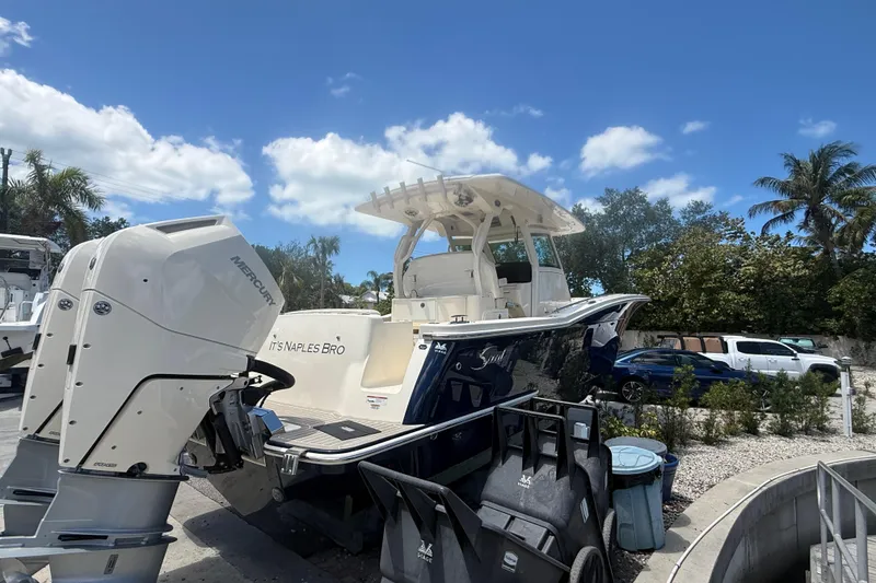 Slide: The Image of 2025 Scout 330 LXF boat with Mercury engine, parked outdoors under a clear blue sky. - 4