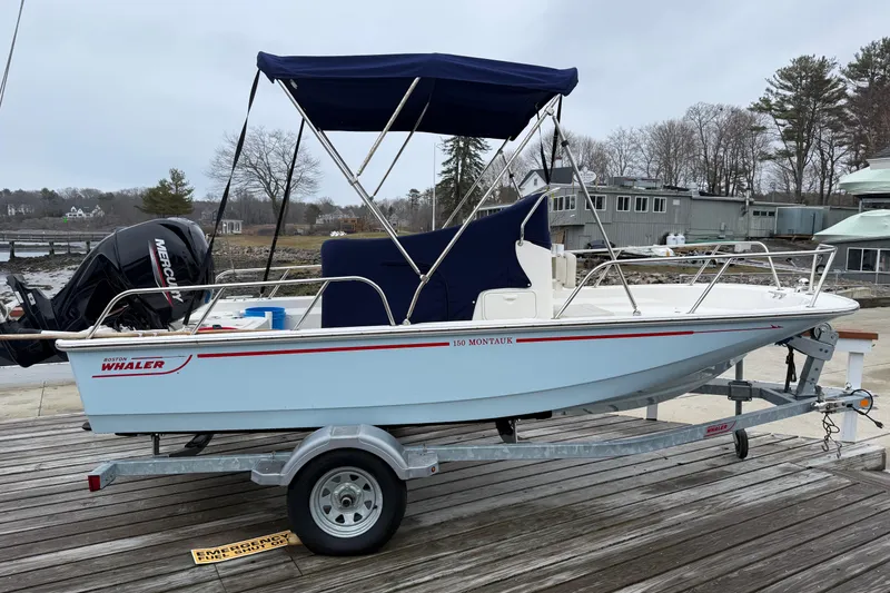 Slide: The Image of 2021 Boston Whaler 150 Montauk boat on trailer, docked near waterfront buildings. - 8