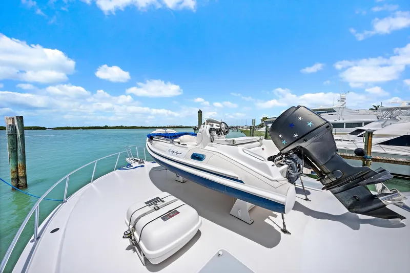 Slide: The Image of A Viking 55 Convertible yacht with a small boat on deck, docked by clear blue waters. - 16