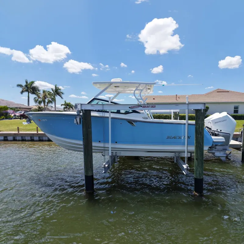 The Image of 2023 Blackfin 272 DC boat on lift, blue hull, Mercury engine, sunny day, waterfront view. - 0