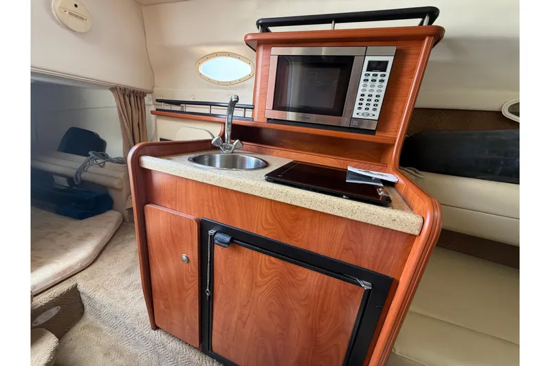 Slide: The Image of 2006 Rinker 250 Express Cruiser interior kitchenette with microwave, sink, and compact fridge. - 24