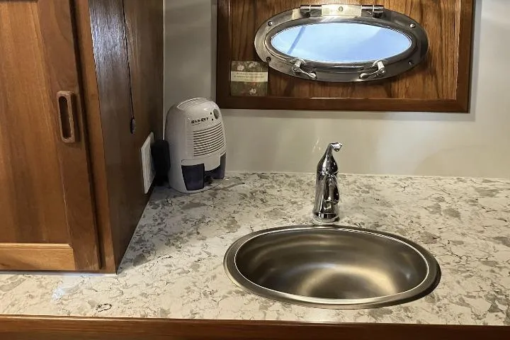 Slide: The Image of Compact bathroom sink with marble countertop, wooden cabinet, and porthole window in a 1990 Cooper Prowler Sedan. - 17
