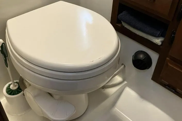 Slide: The Image of White RV toilet with foot pedal, adjacent storage, and cleaning brush. - 70