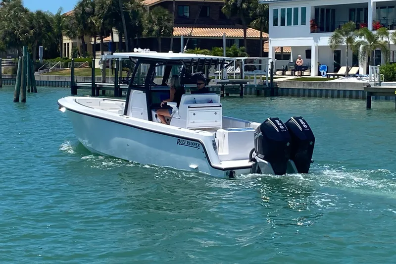 Slide: The Image of 2026 Reef Runner 280 boat cruising on clear blue water near waterfront homes. - 2