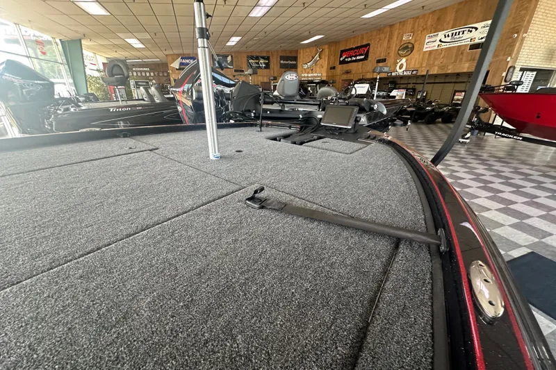 Slide: The Image of 2026 Triton 20XP Patriot boat displayed in showroom with carpeted deck and fishing equipment. - 136