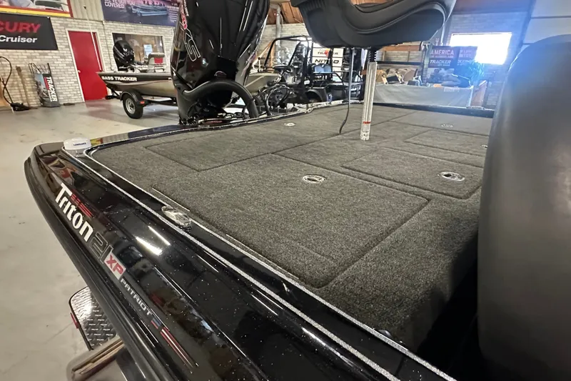 Slide: The Image of 2025 Triton 21XP Patriot boat interior with carpeted deck and seating in showroom. - 12