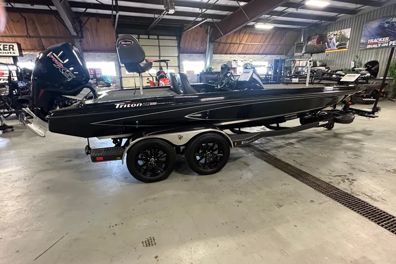 Slide: The Image of 2025 Triton 21XP Patriot boat in showroom, featuring sleek black design and dual-axle trailer. - 2