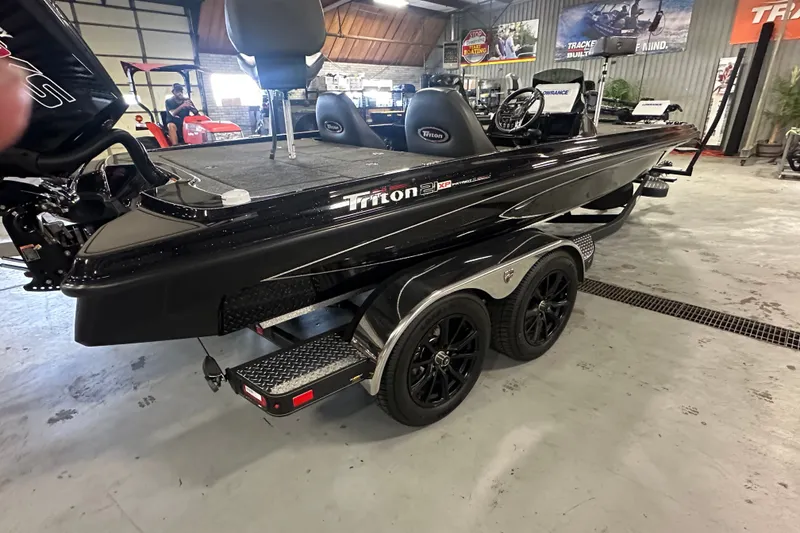 Slide: The Image of 2025 Triton 21XP Patriot boat in showroom, featuring sleek black design and dual-axle trailer. - 3