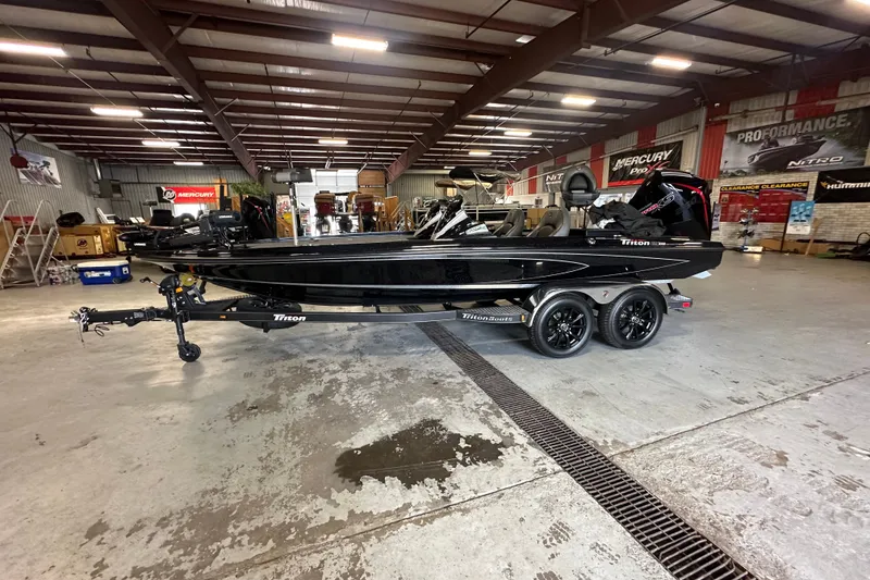 The Image of 2025 Triton 21XP Patriot boat in showroom, sleek black design, dual-axle trailer. - 0