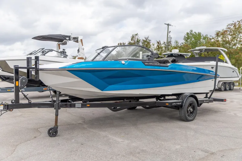 Slide: The Image of 2021 Nautique Ski Nautique boat in blue and white on a trailer, parked outdoors. - 13