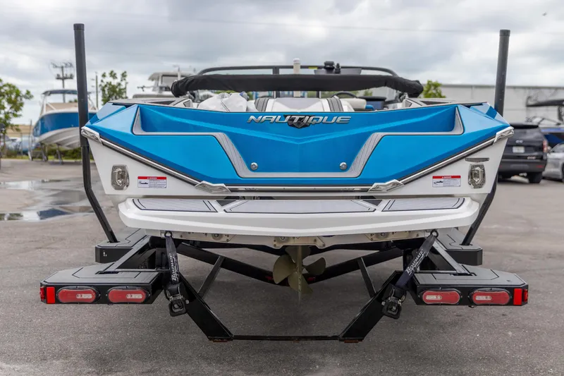Slide: The Image of 2021 Nautique Ski Nautique boat rear view, blue and white design, parked outdoors. - 14