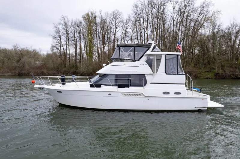 Slide: The Image of 2000 Carver 404 Cockpit Motor Yacht on a serene river with forested background. - 55