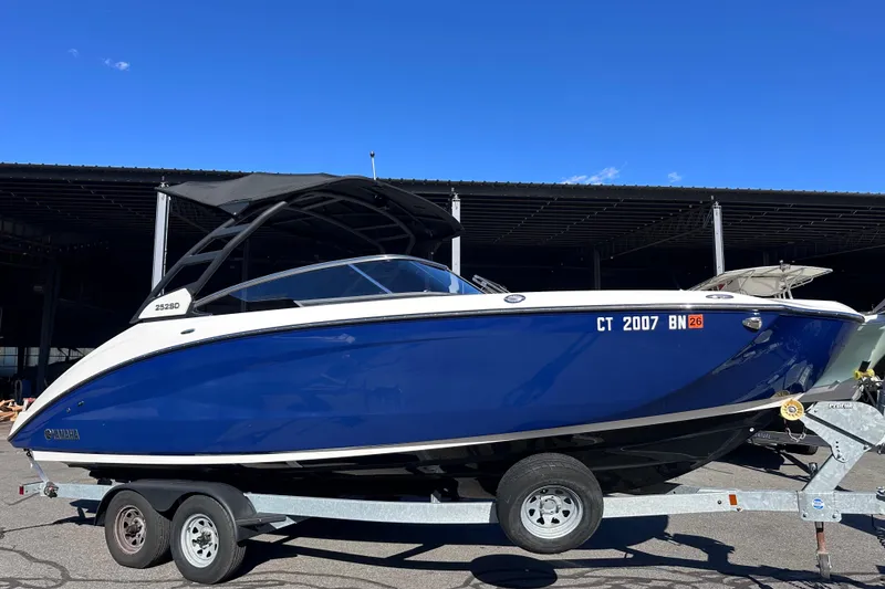 Slide: The Image of 2021 Yamaha Boats 252SD on trailer, blue hull, parked outdoors under clear sky. - 2