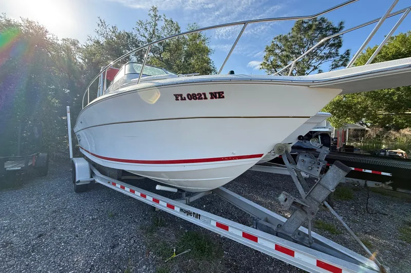 Slide: The Image of 2000 Sport-Craft 241 Walk Around boat on trailer, parked outdoors with sunlight filtering through trees. - 7