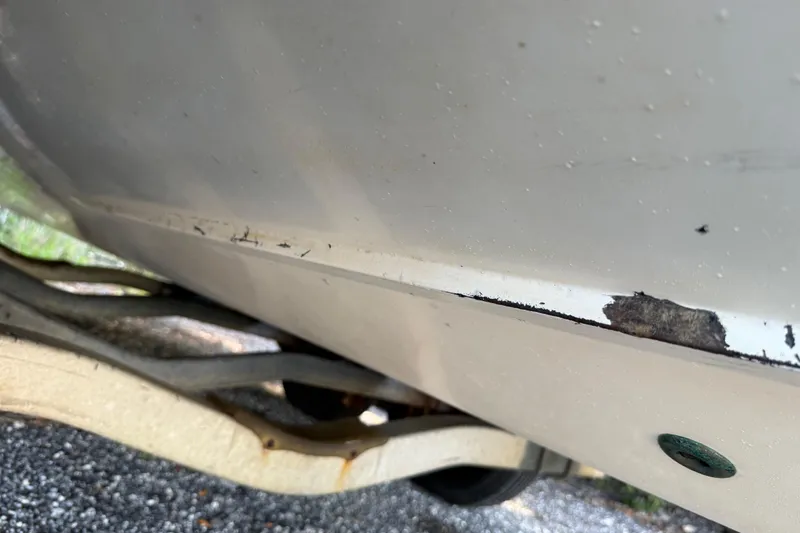 Slide: The Image of Close-up of 2000 Sport-Craft 241 Walk Around boat hull with visible wear and damage. - 99