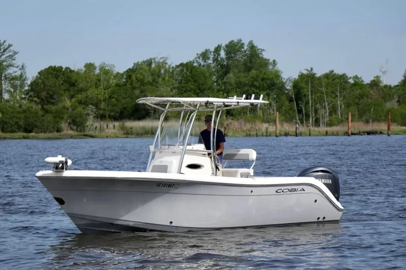 Slide: The Image of 2019 Cobia 220 Center Console boat cruising on a calm lake with lush greenery. - 3