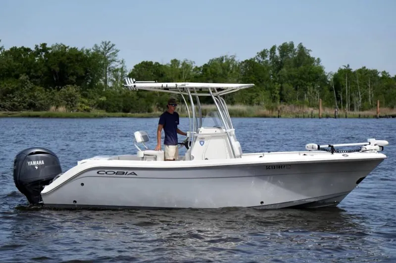 Slide: The Image of 2019 Cobia 220 Center Console boat on water with Yamaha engine, surrounded by trees. - 1
