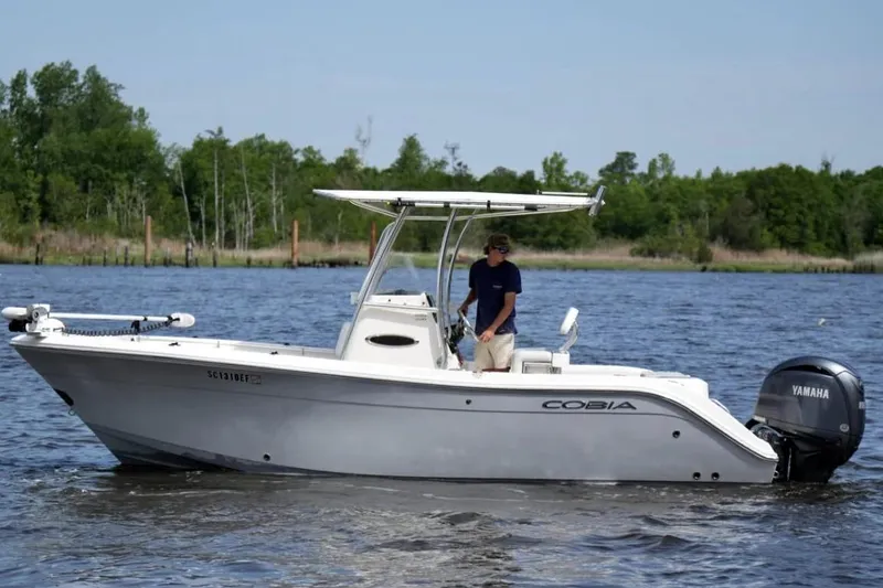 Slide: The Image of 2019 Cobia 220 Center Console boat on water with Yamaha engine, surrounded by trees. - 2