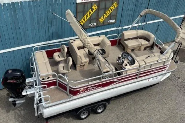 Slide: The Image of 2019 Sun Tracker SportFish 22 DLX pontoon boat with beige seating and red accents, parked on trailer. - 7