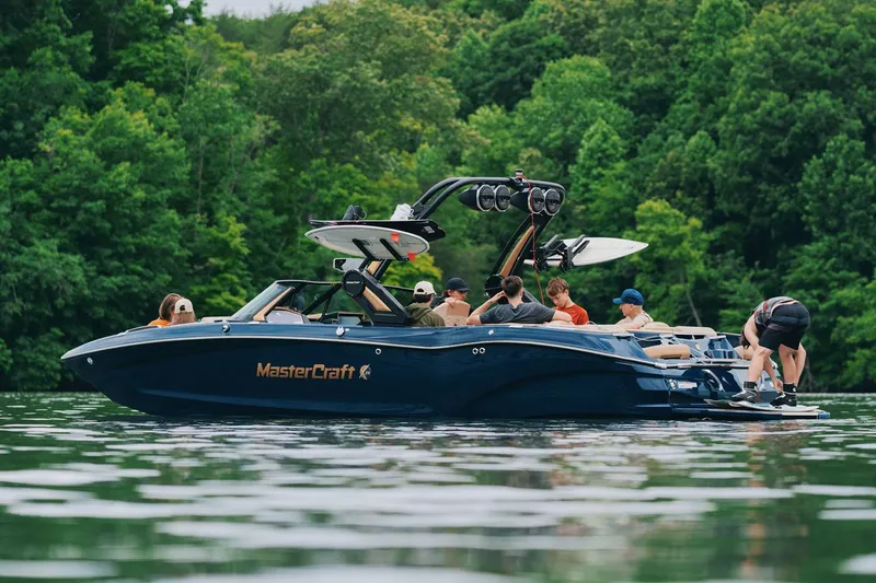 Slide: The Image of Manufacturer Provided Image: 2025 MasterCraft X24 boat on a lake with people, surrounded by lush greenery. - 4