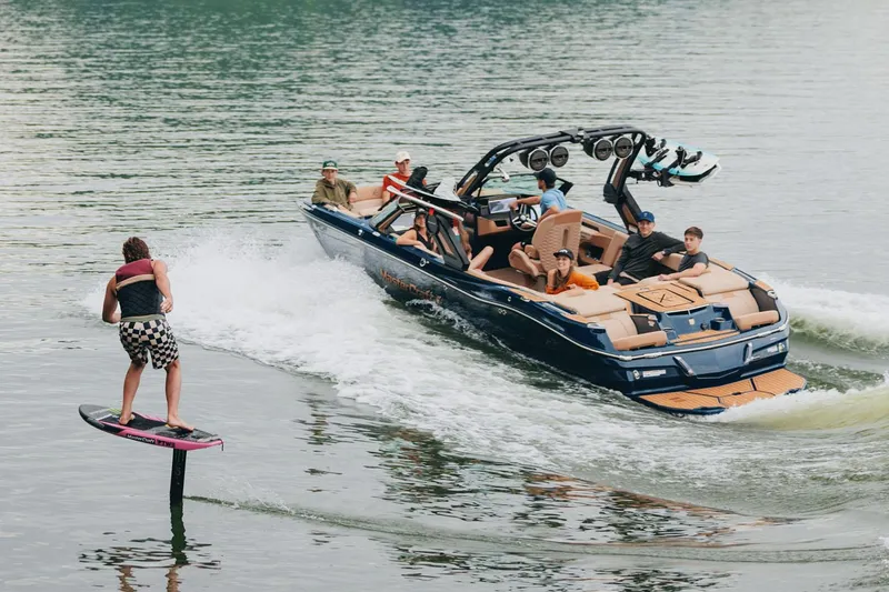 Slide: The Image of Manufacturer Provided Image: 2025 MasterCraft X24 towing a wakeboarder on a lake, with passengers enjoying the ride. - 5