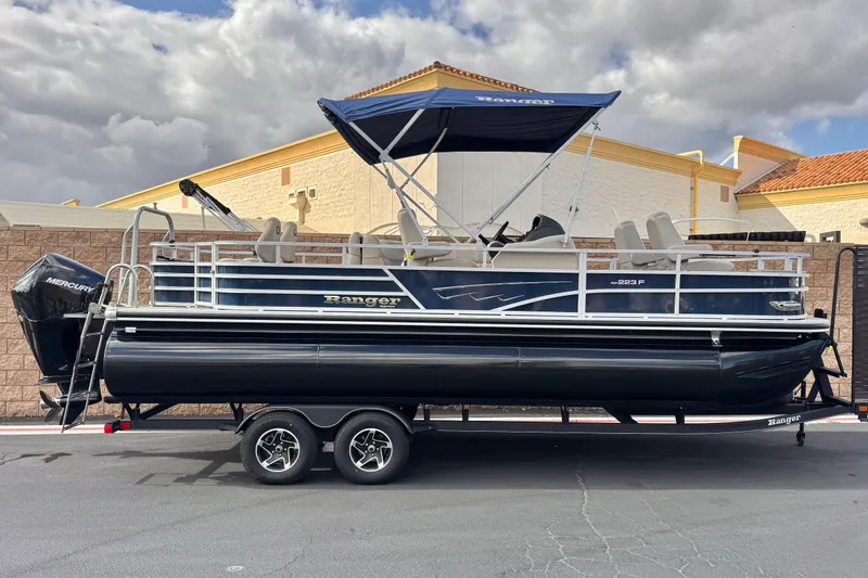 The Image of 2024 Ranger Reata 223F pontoon boat on trailer, parked outdoors under cloudy sky. - 0