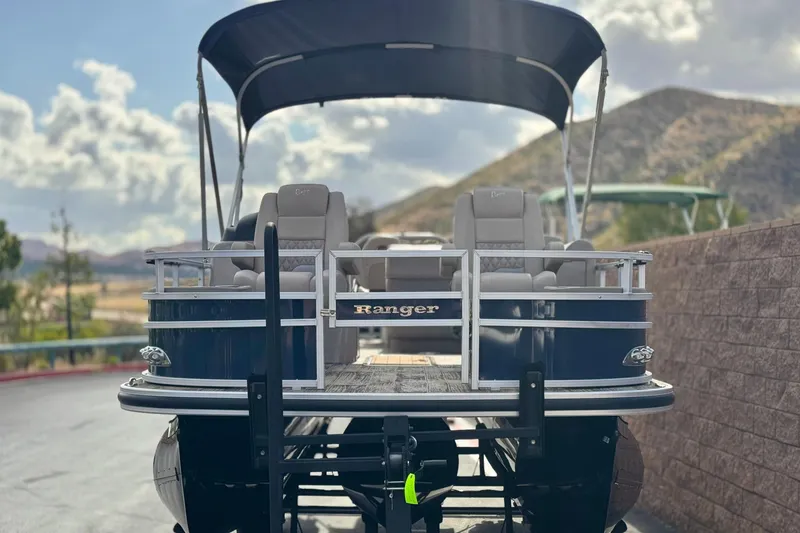 Slide: The Image of 2024 Ranger Reata 223F pontoon boat with canopy, parked outdoors against scenic hills. - 2