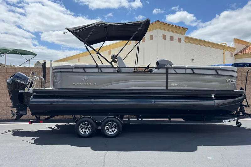 The Image of 2024 Regency 230 DL3 pontoon boat on trailer under blue sky. - 0